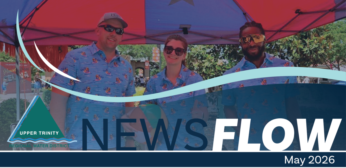 Group of three smiling people in matching blue shirts at an outdoor event under a pink canopy, with a 'NEWS FLOW' banner and the Upper Trinity Regional Water District logo in the foreground.